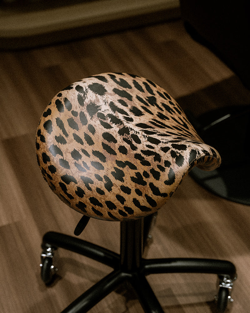Stella - black saddle stool with leopard upholstery and roller wheels